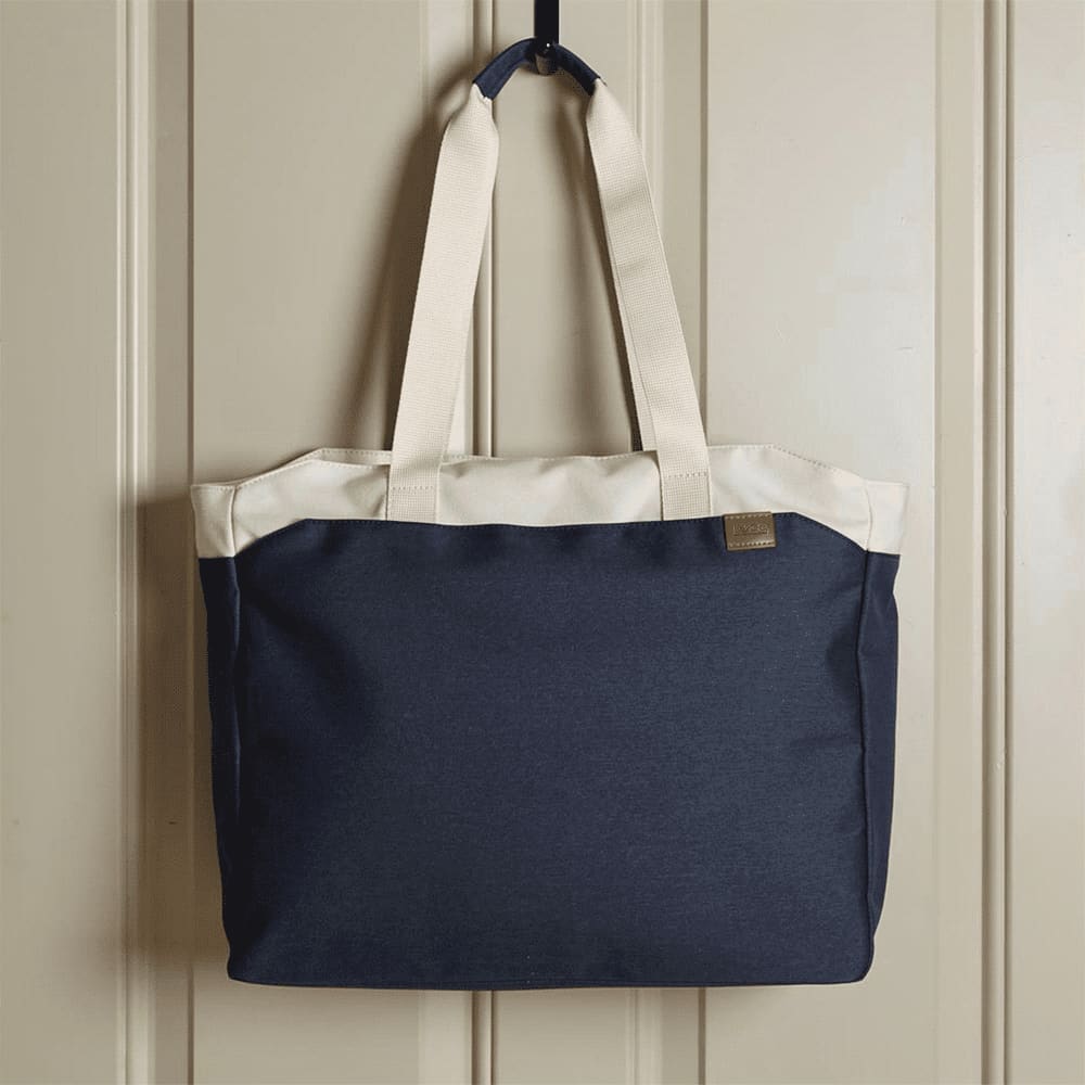 A navy blue tote bag with cream handles, featuring a logo on the front, hanging against a wall.