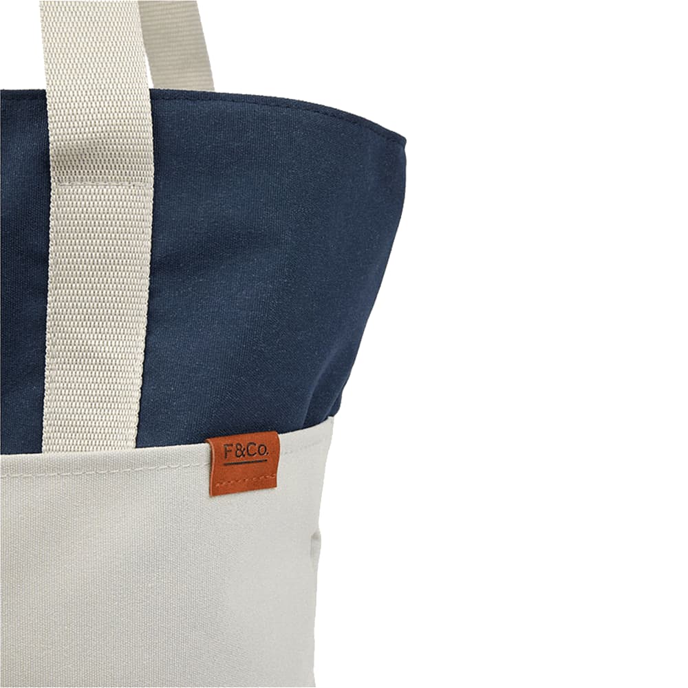 A tote bag featuring a navy blue top and a cream bottom, with a small logo tag.