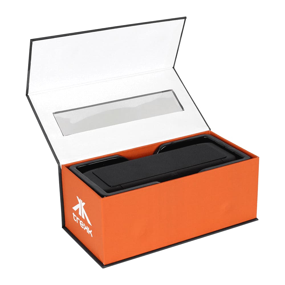 A black outdoor speaker and wireless power bank in an open orange box with a clear plastic window and branding.
