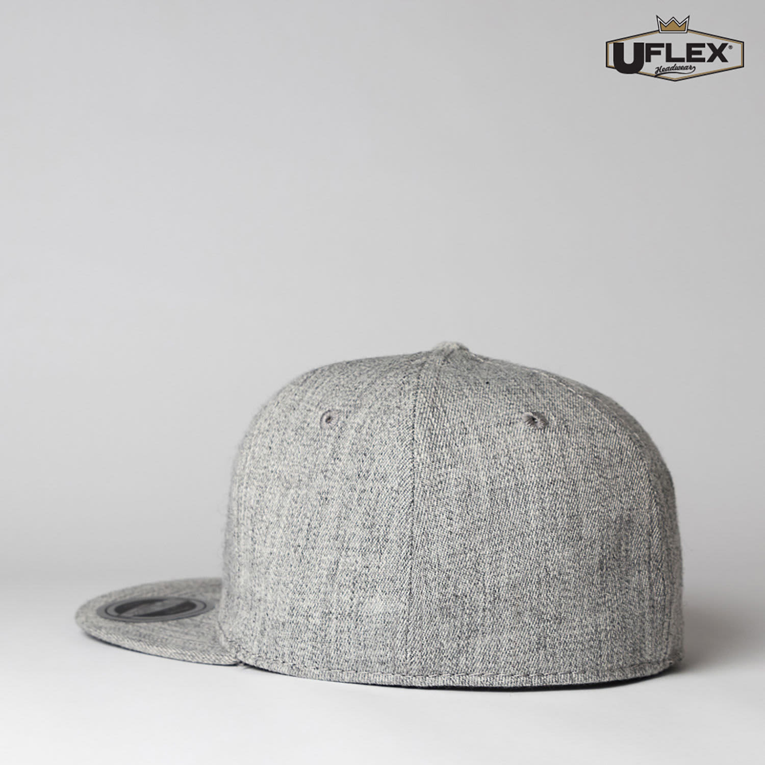 A grey fitted cap with a flat peak and six panels, featuring a logo on the side.