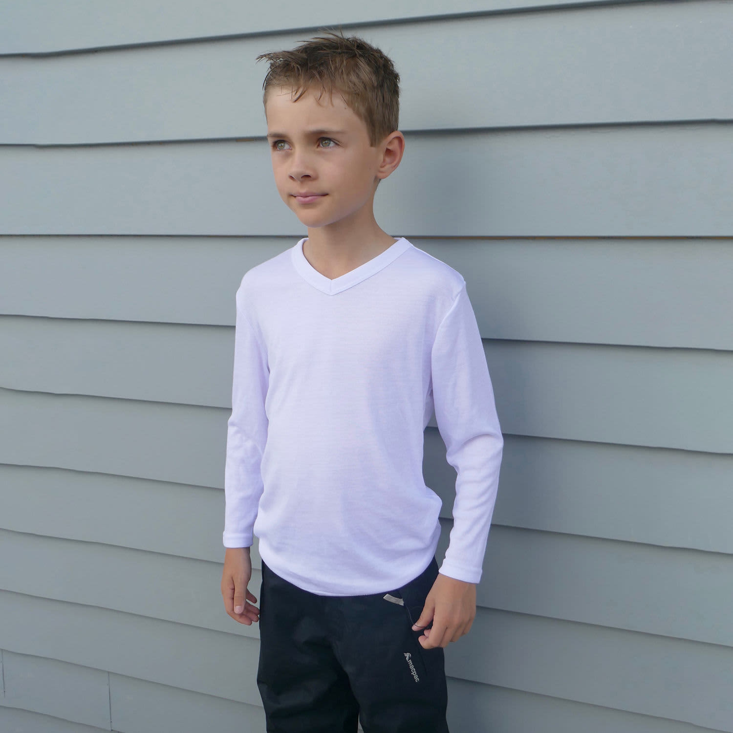 A youth in a white longsleeve V-neck thermal shirt stands against a grey wall. The shirt features a branding logo.