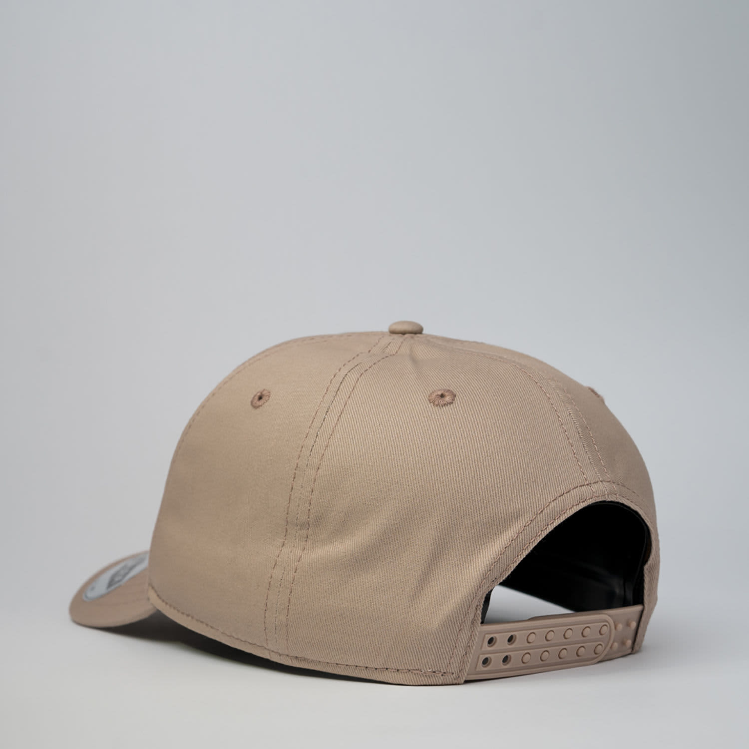 A tan five-panel snapback cap with a branded logo and an adjustable strap at the back.