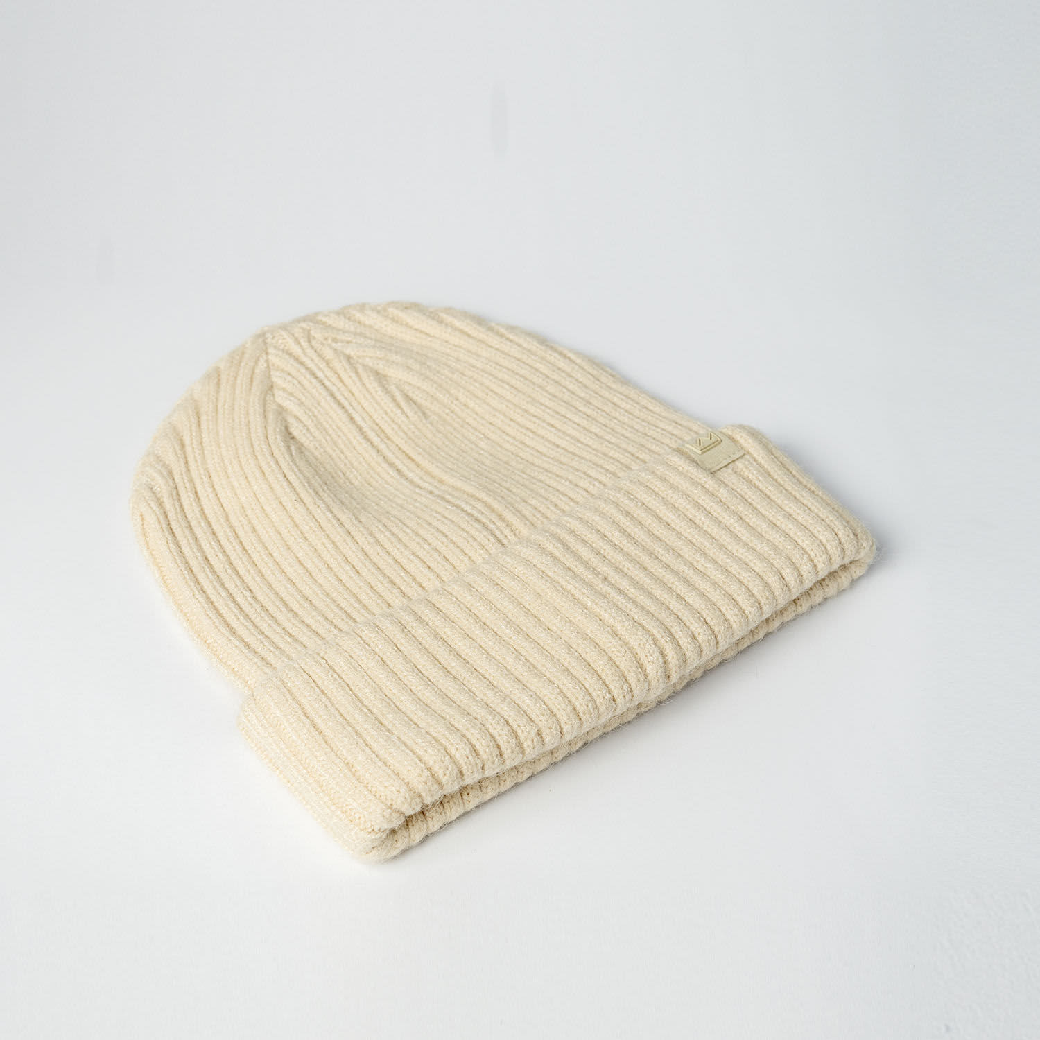 A cream-coloured beanie with a ribbed texture and a small logo. It features a folded cuff design.