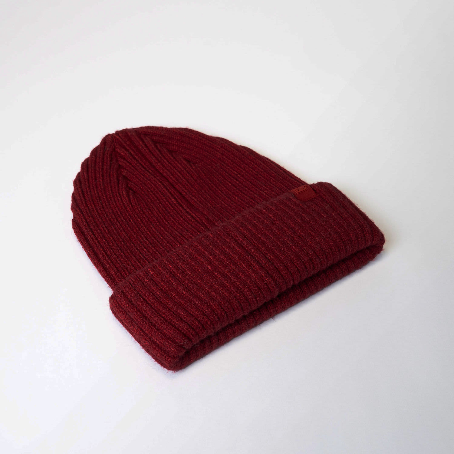 A maroon Fisherman's Beanie with a ribbed texture and a folded cuff, featuring a logo.