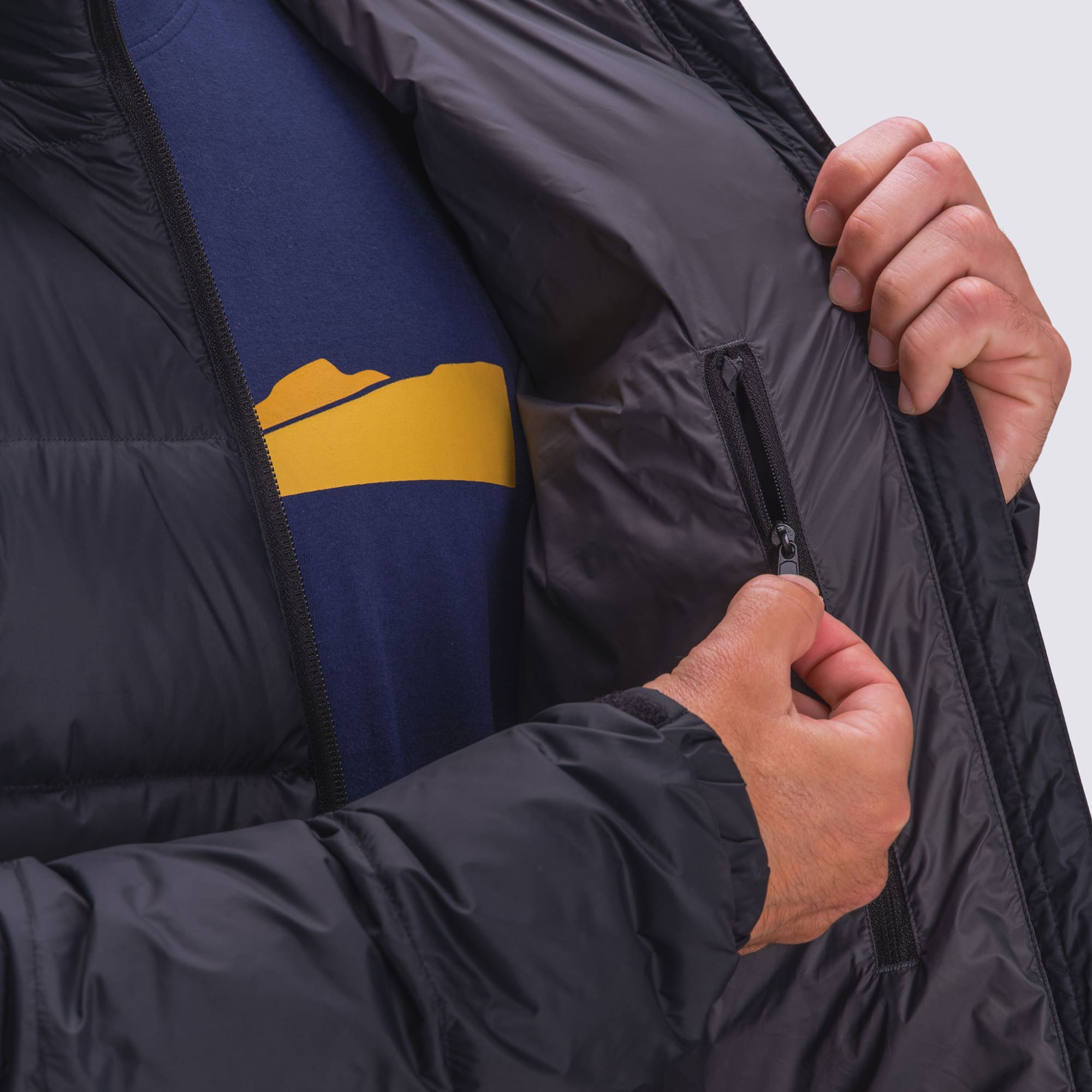A puffer jacket in black with a zippered inner pocket, being worn over a navy blue shirt featuring a mountain design.