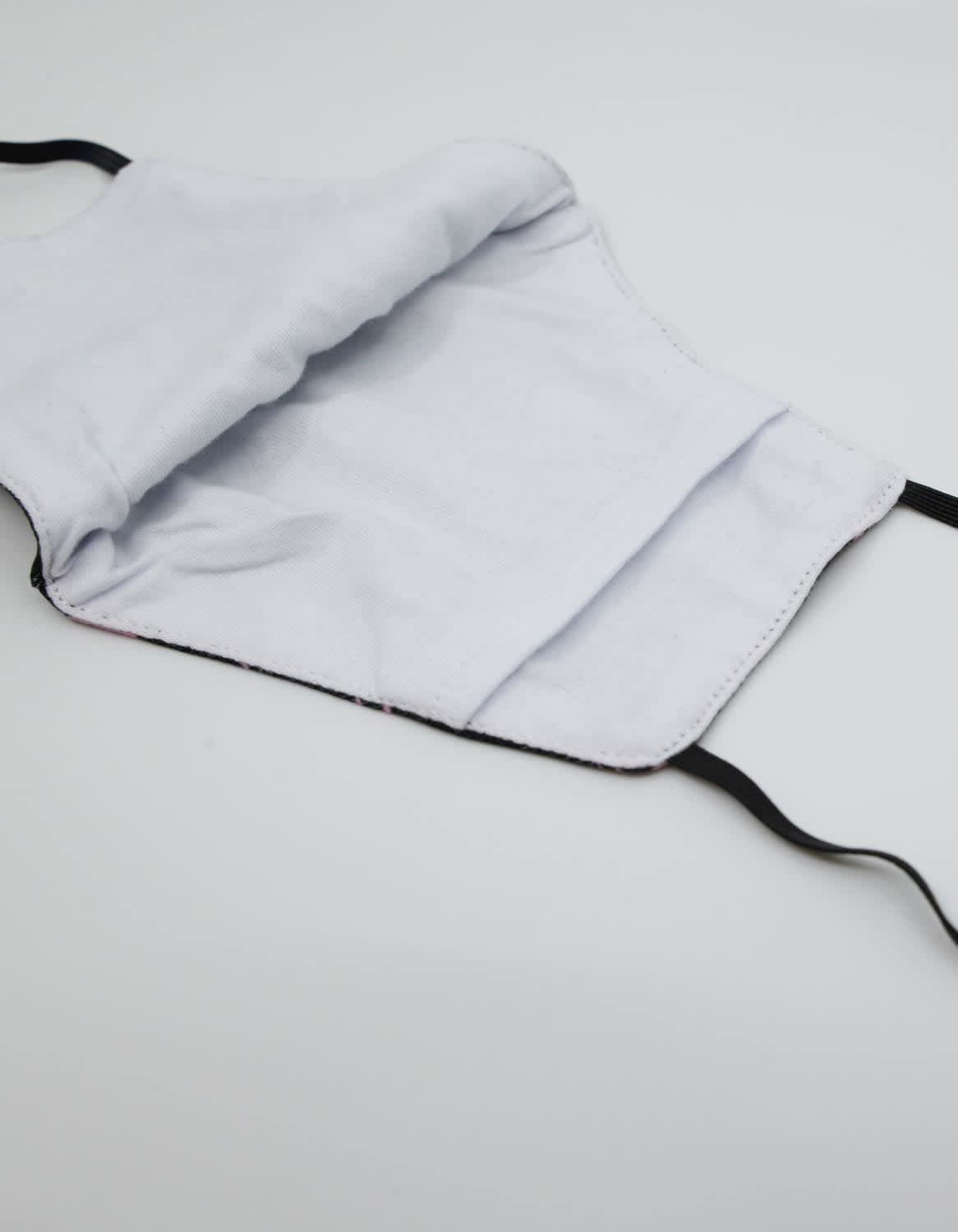 A black face mask made from 100% cotton with an inner lining showing. It features elastic ear straps and a label.