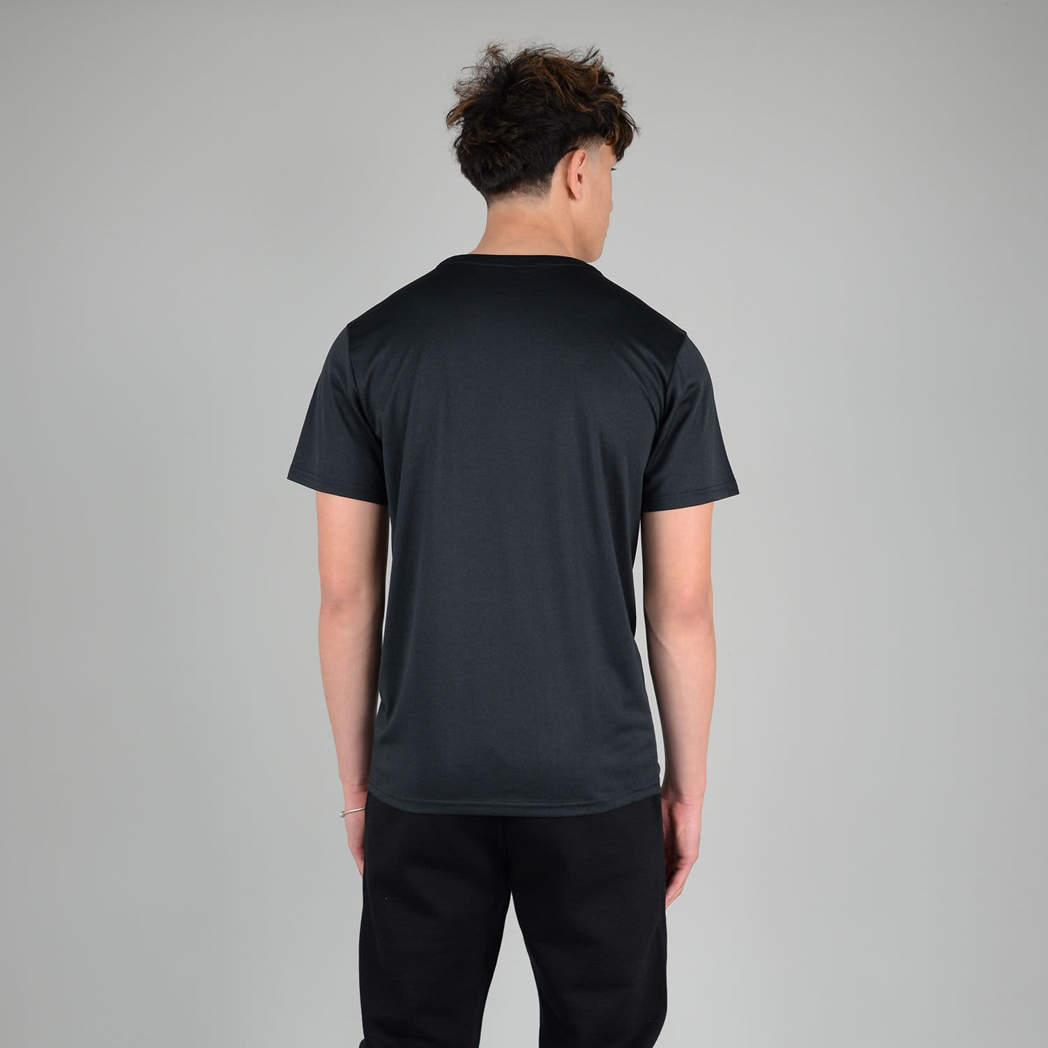 A black adult tech tee featuring a simple design and a logo on the back, worn by a model from behind.