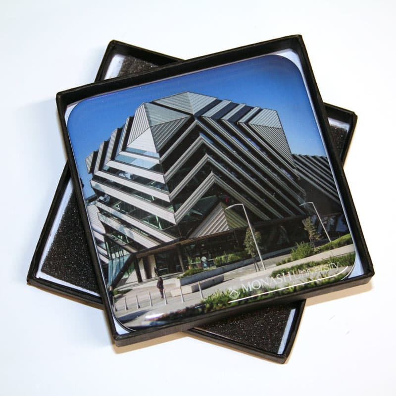 A set of full colour epoxy domed coasters featuring a modern building design, packaged in a black box with foam.