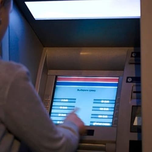A person using an ATM with a touchscreen display and various selection options visible.