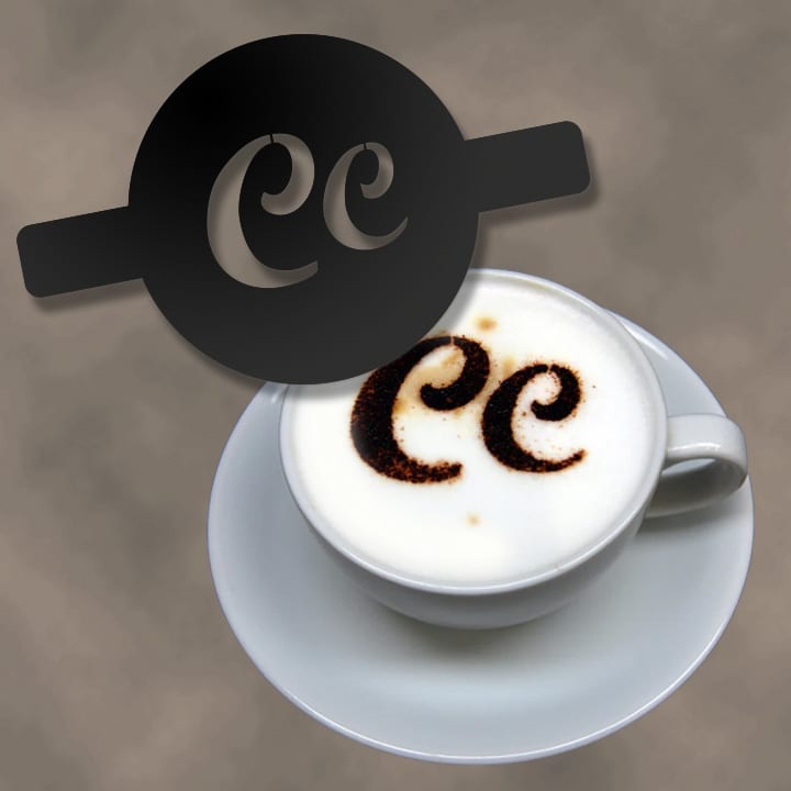A coffee cup with frothed milk topped with cocoa powder designs, featuring a black stencil above it.