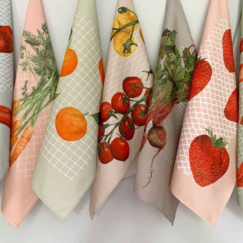 Custom cotton tea towels in various pastel colours featuring illustrations of fruits and vegetables.