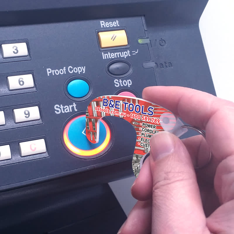 A transparent tool with an orange design, being used to press a button on a machine. It has a logo.