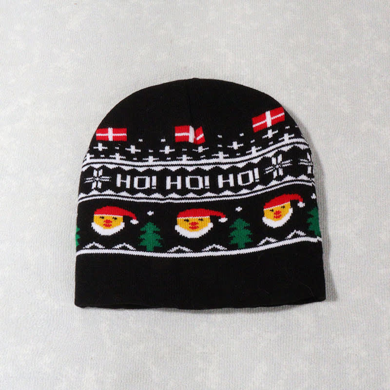 A black knitted beanie featuring festive designs, including smiling Santa faces and snowflakes. It has a logo.