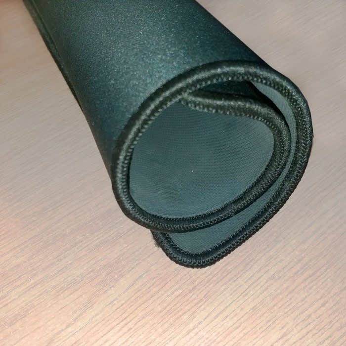 A black deluxe overlocked fabric mousepad, rolled up, showing the textured surface and stitched edges.