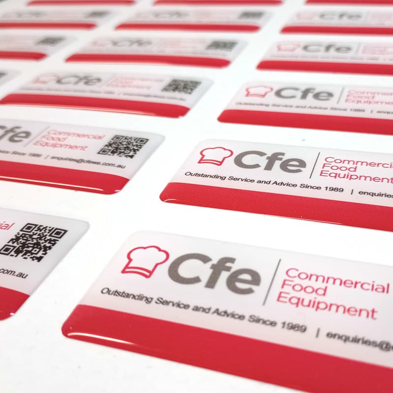 Glossy red and white dome stickers featuring a logo and QR code, arranged on a white surface.