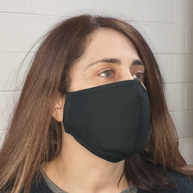 A woman wearing a black, deluxe 3-ply fabric face mask. The mask appears fitted and has a simple design.