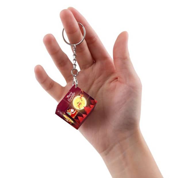 A hand holding a small, cube-shaped keyring with vibrant colours and a logo, attached to a silver chain.