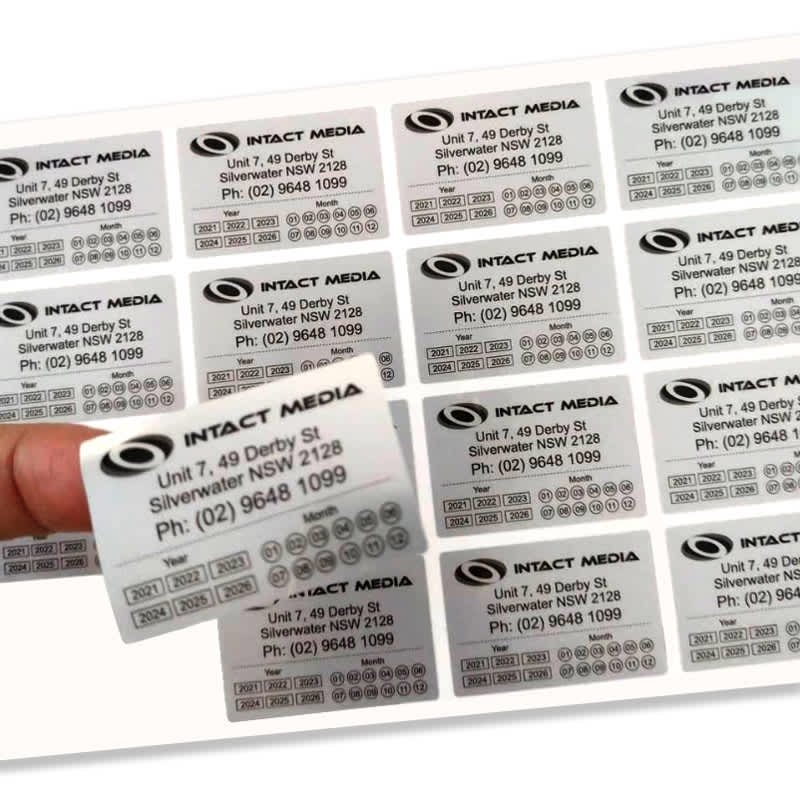 A hand holding a white sticker sheet featuring multiple rectangular stickers with black text and a logo.