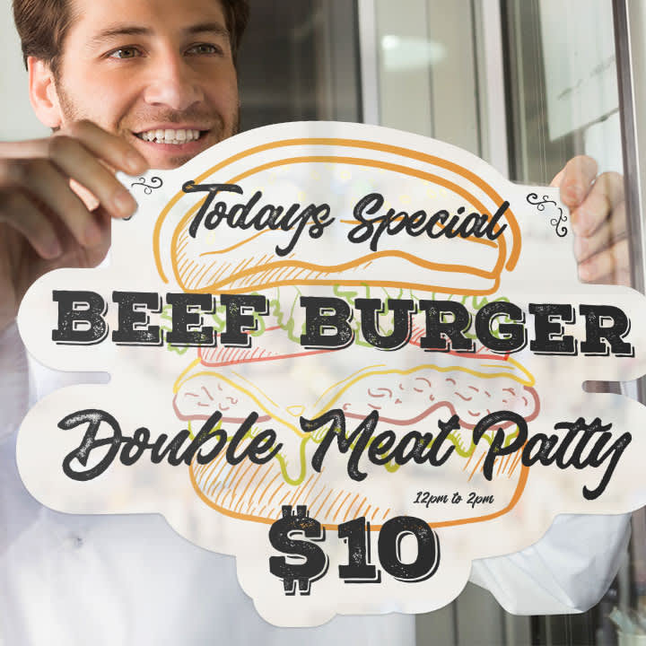 A person is placing a colourful static cling decal of a beef burger with text on a glass surface.