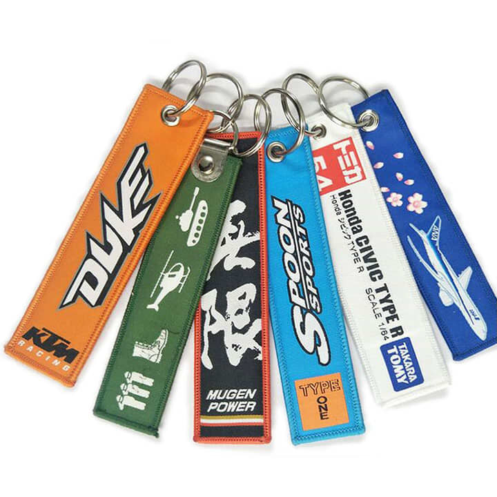 A collection of woven keyrings in various colours, featuring different designs and a logo on some.
