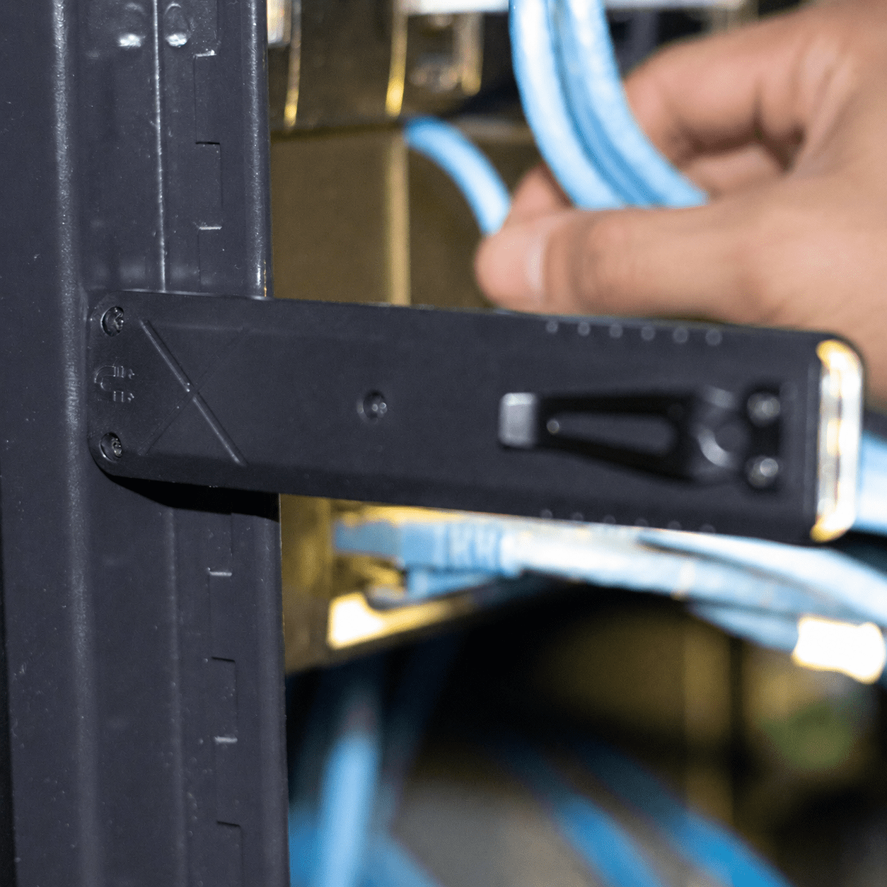 A black tool with a handle and measurement markings, positioned near blue cables in a rack.
