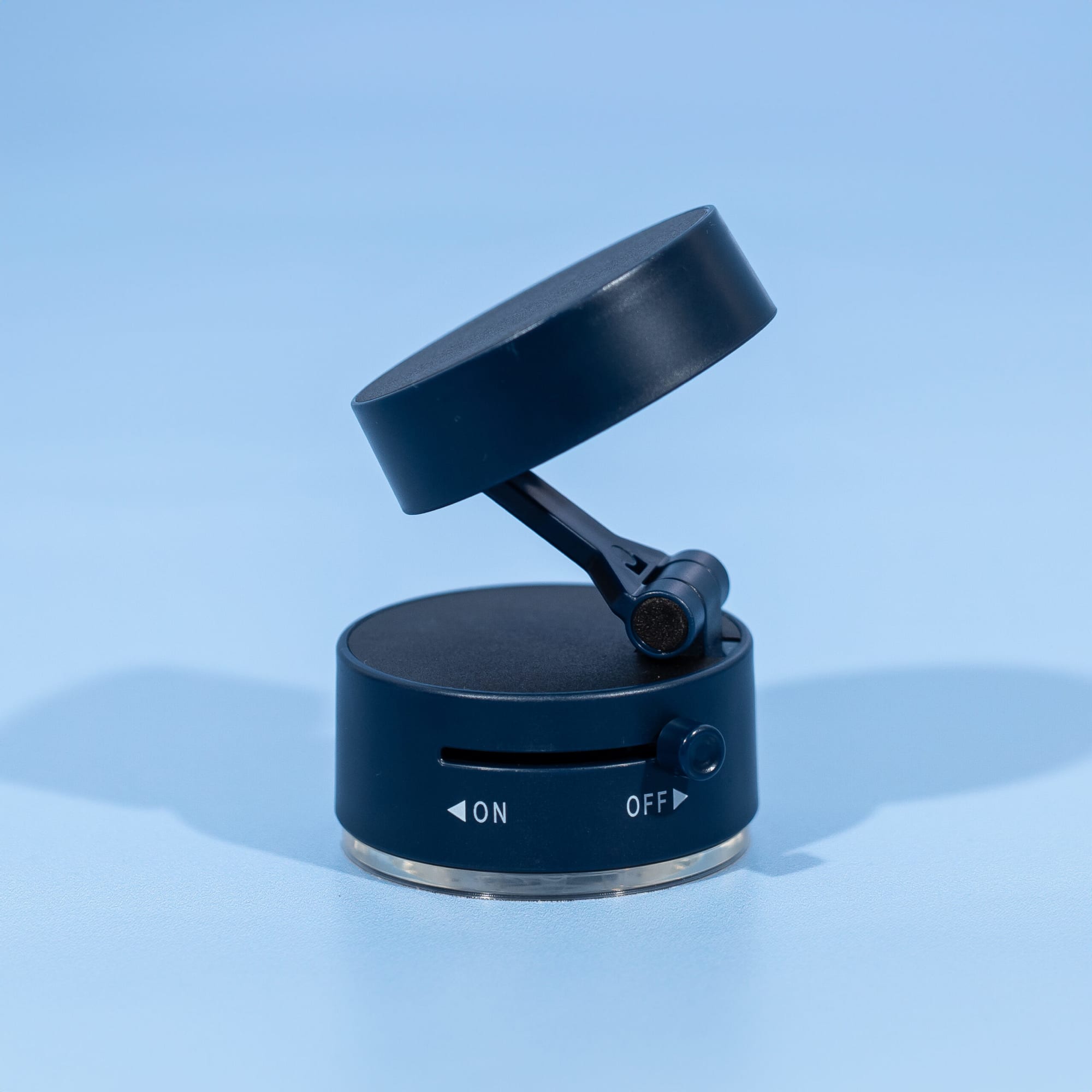 A black and silver vacuum suction phone stand with a rotating top and an on/off switch. It features a logo.