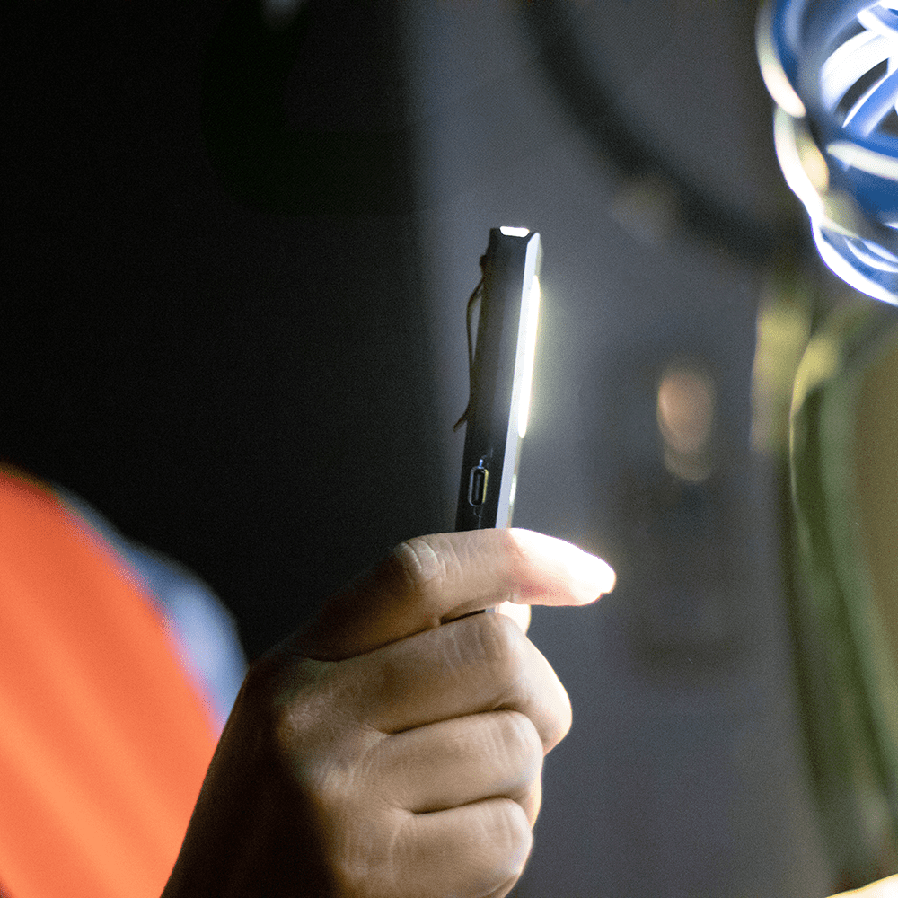 A handheld rechargeable work light with a bright white LED, set against a dark background, featuring a sleek black design.