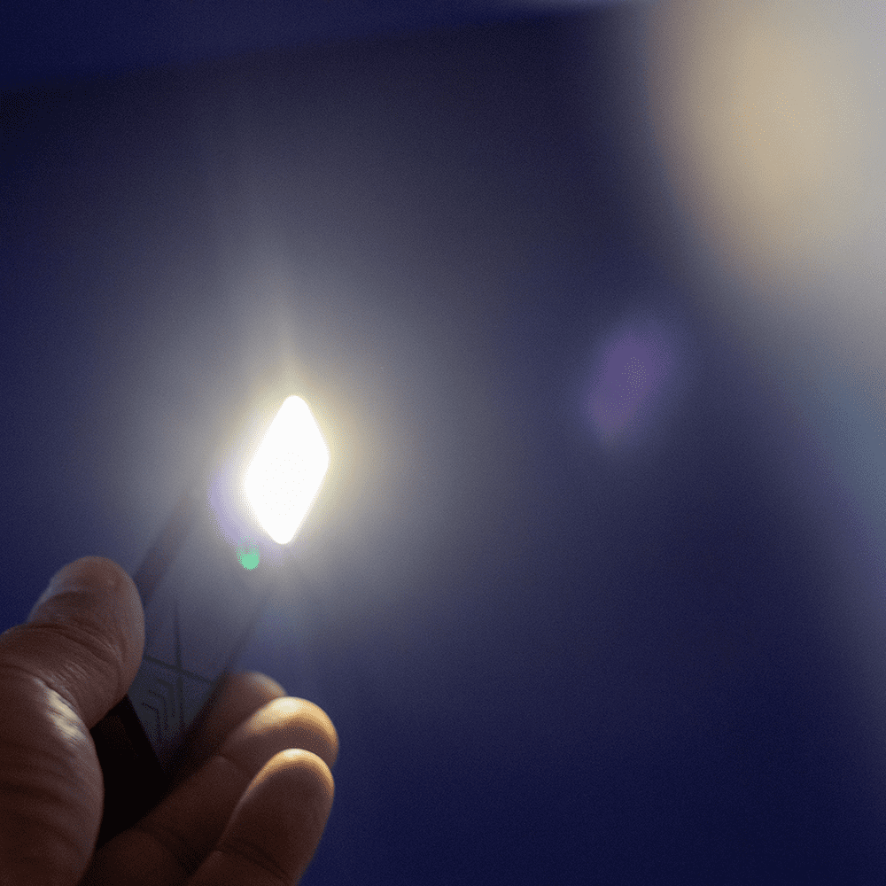 A handheld rechargeable work light emits a bright white light against a blue background. It features a logo on its surface.