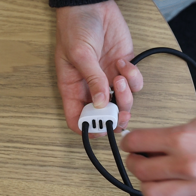 A black charging lanyard with a white connector, being adjusted in a person's hands on a wooden surface.