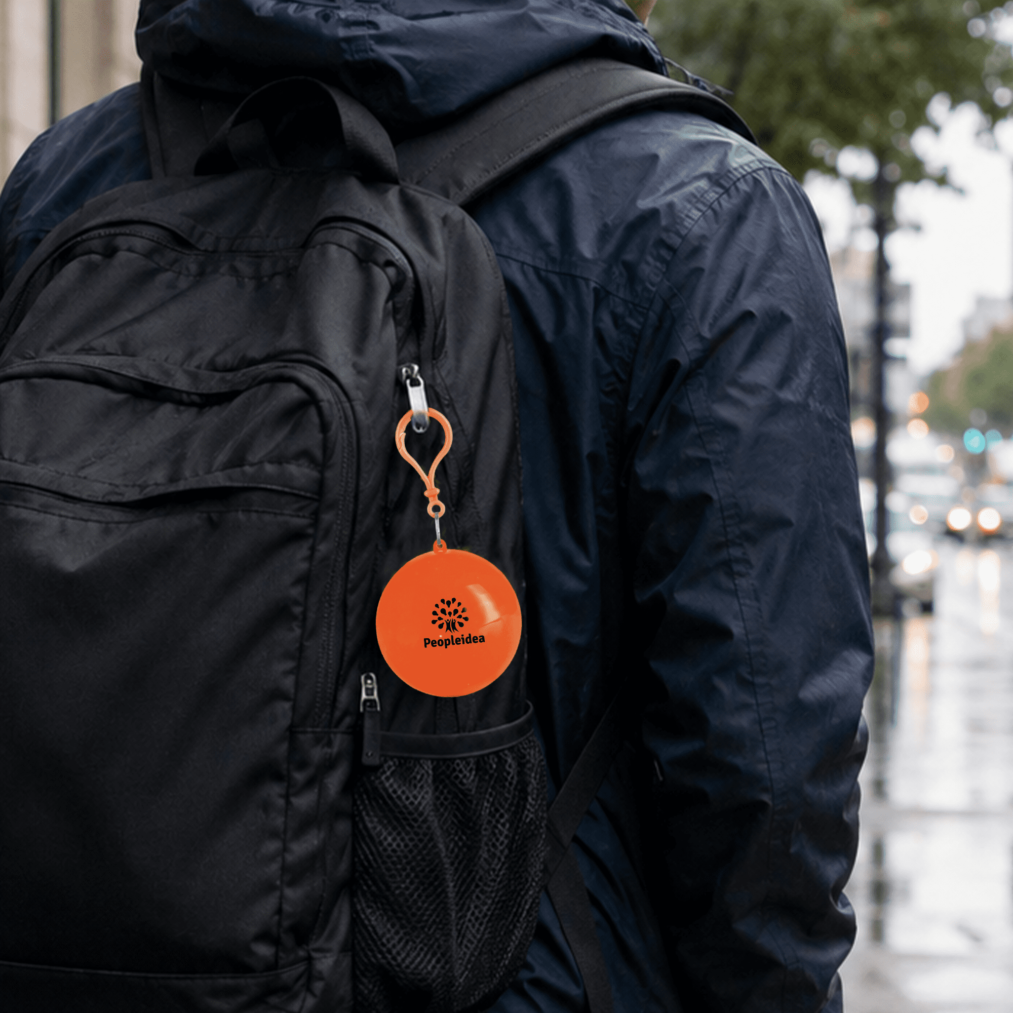 An orange rain poncho ball attached to a black backpack, showcasing a compact and portable design.