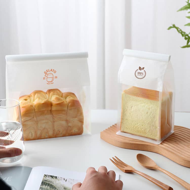 Clear sealing storage bags in a white and orange design, containing loaves of bread on a wooden tray.