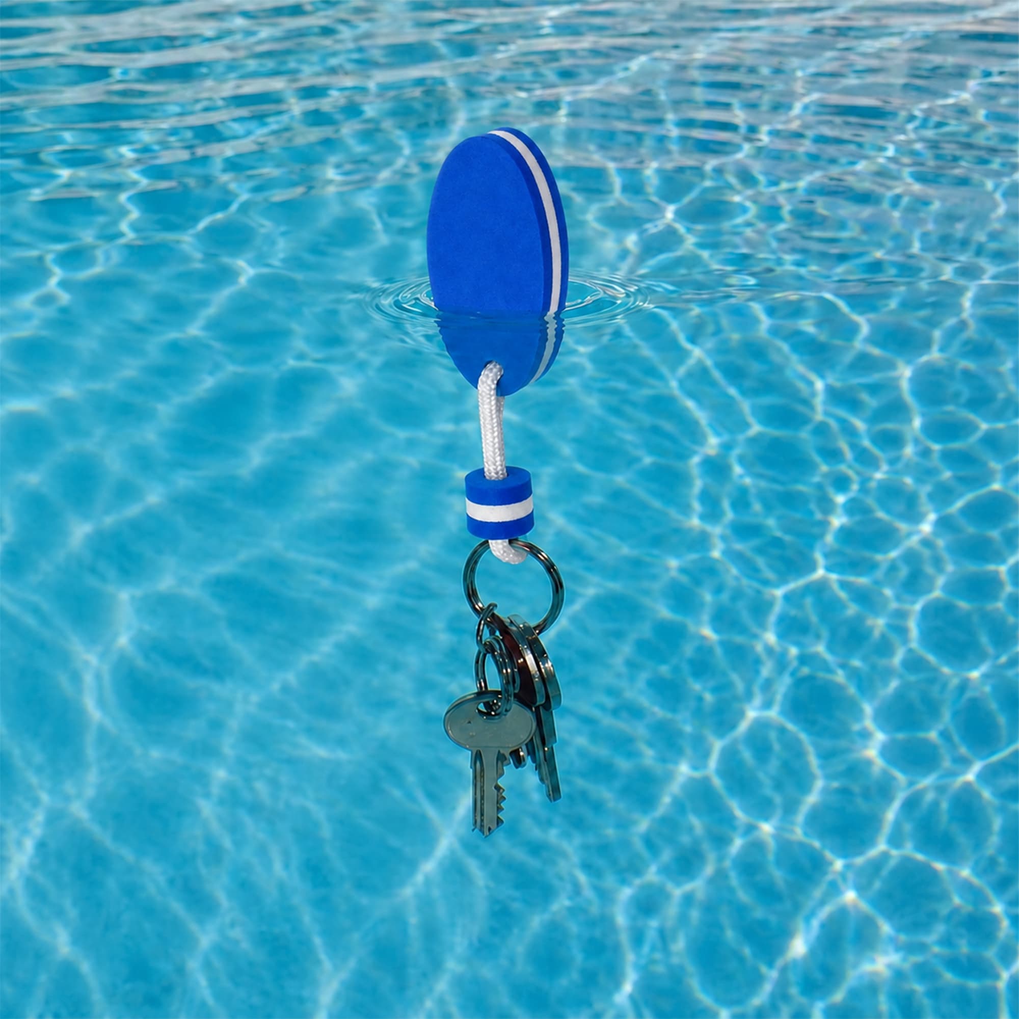 A blue EVA floating keychain with keys attached, floating on the surface of a clear blue pool.