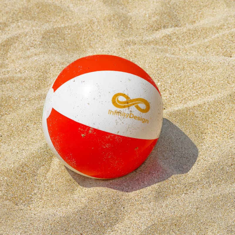 An inflatable beach ball in red and white, resting on sandy beach. It features a logo on one side.