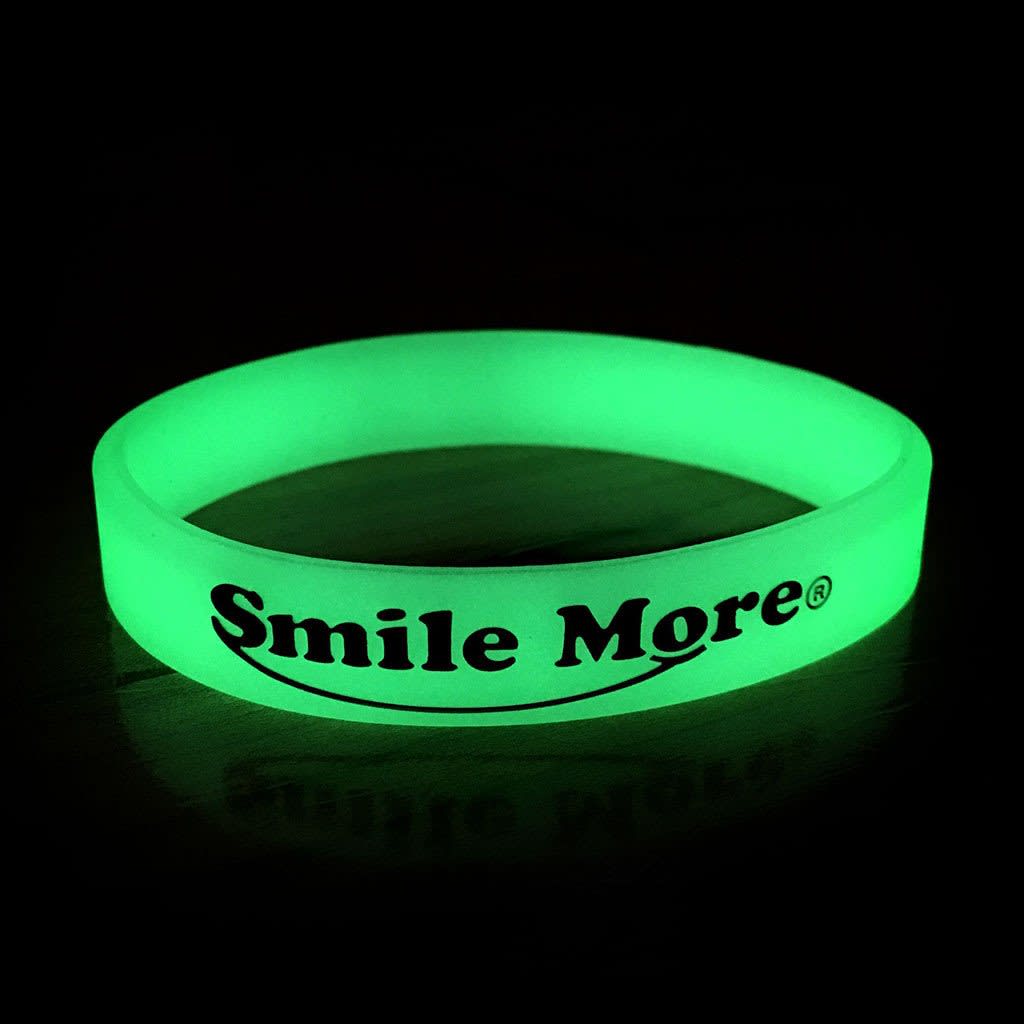 A green glow in the dark wristband with a logo, displayed against a dark background.