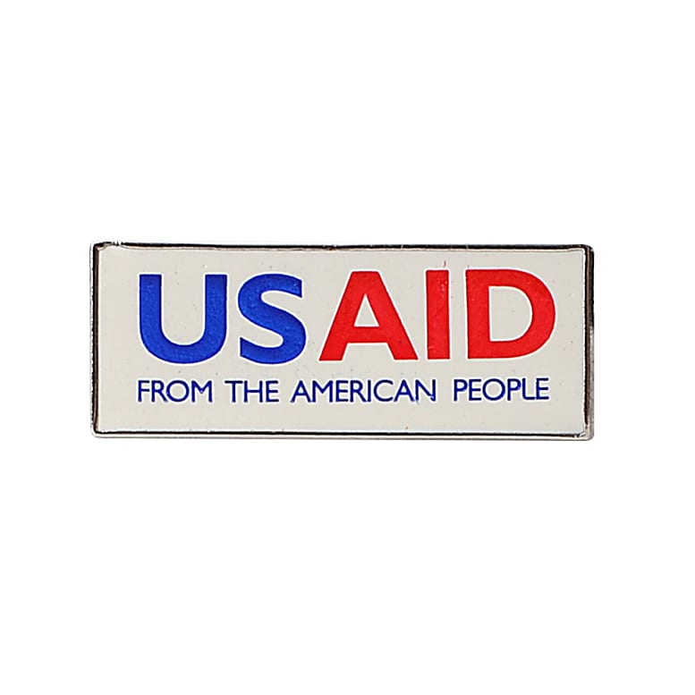 A rectangular lapel pin in blue, red, and white colours featuring a logo and text.