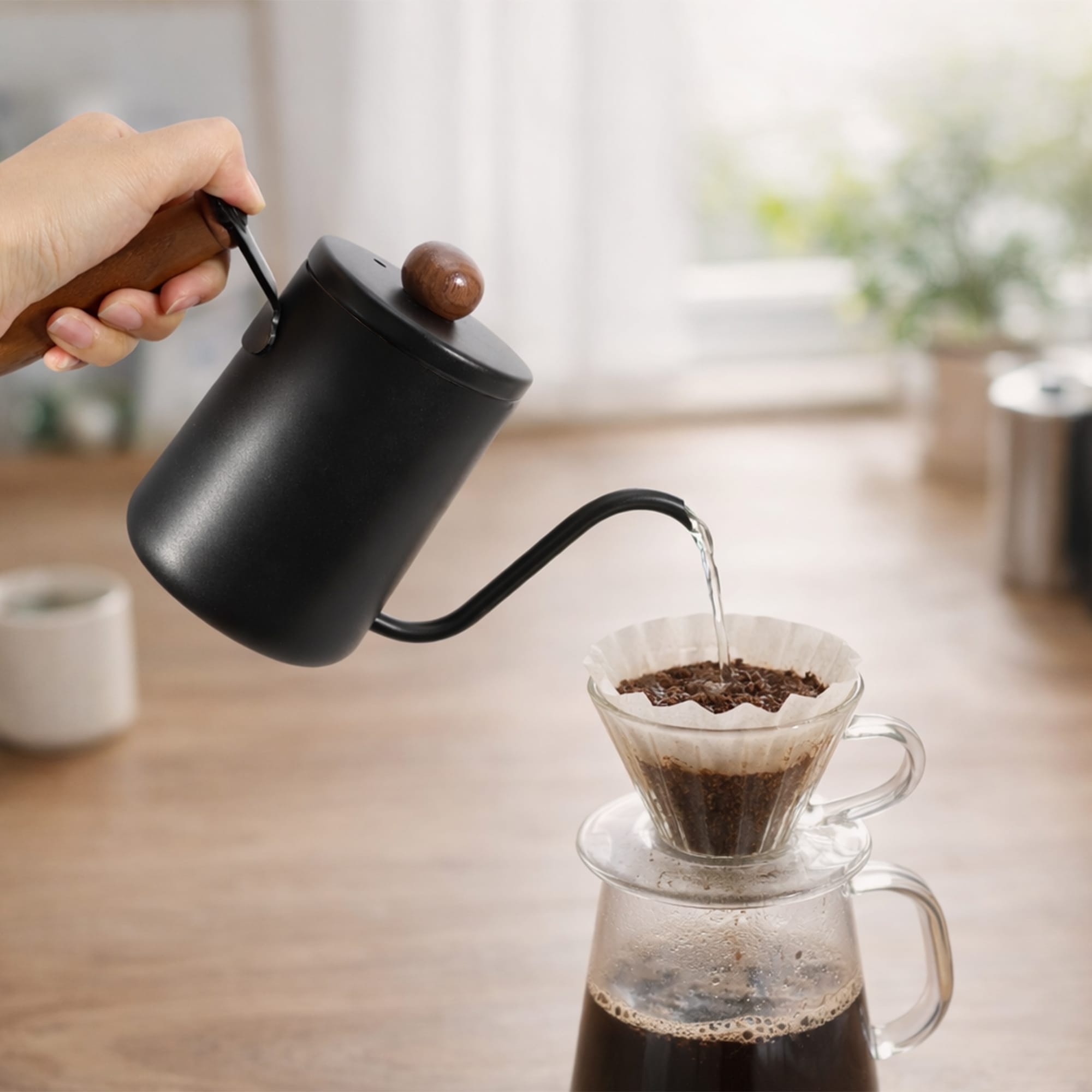 A stainless steel pour over kettle with a wooden handle in black, pouring water into a coffee filter.
