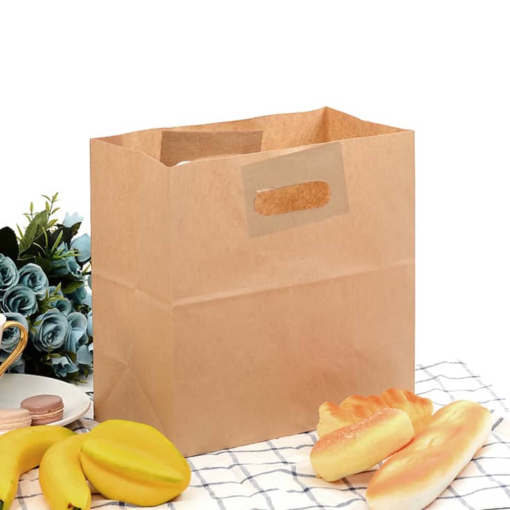A brown kraft paper bag with handles, surrounded by bananas, pastries, and a decorative plant.