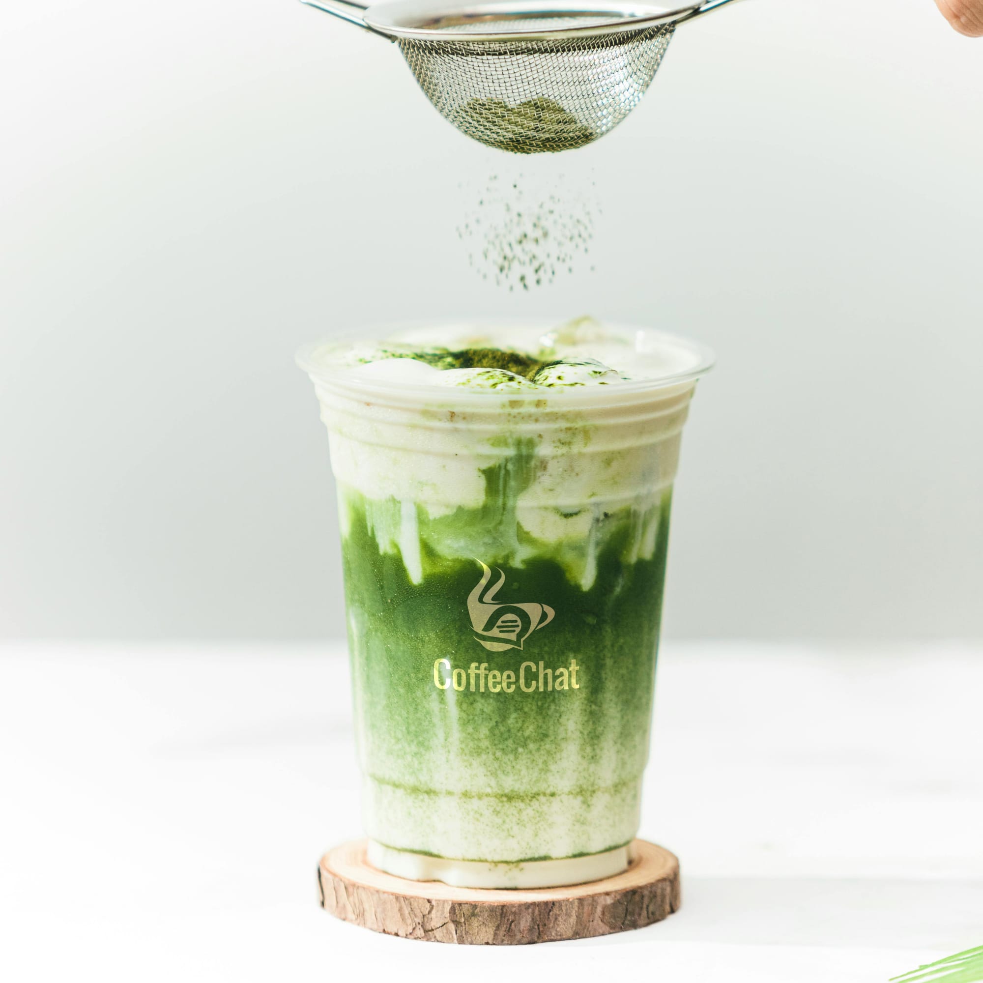 A clear plastic cup filled with a green drink and topped with frothy cream, featuring a logo on the cup.