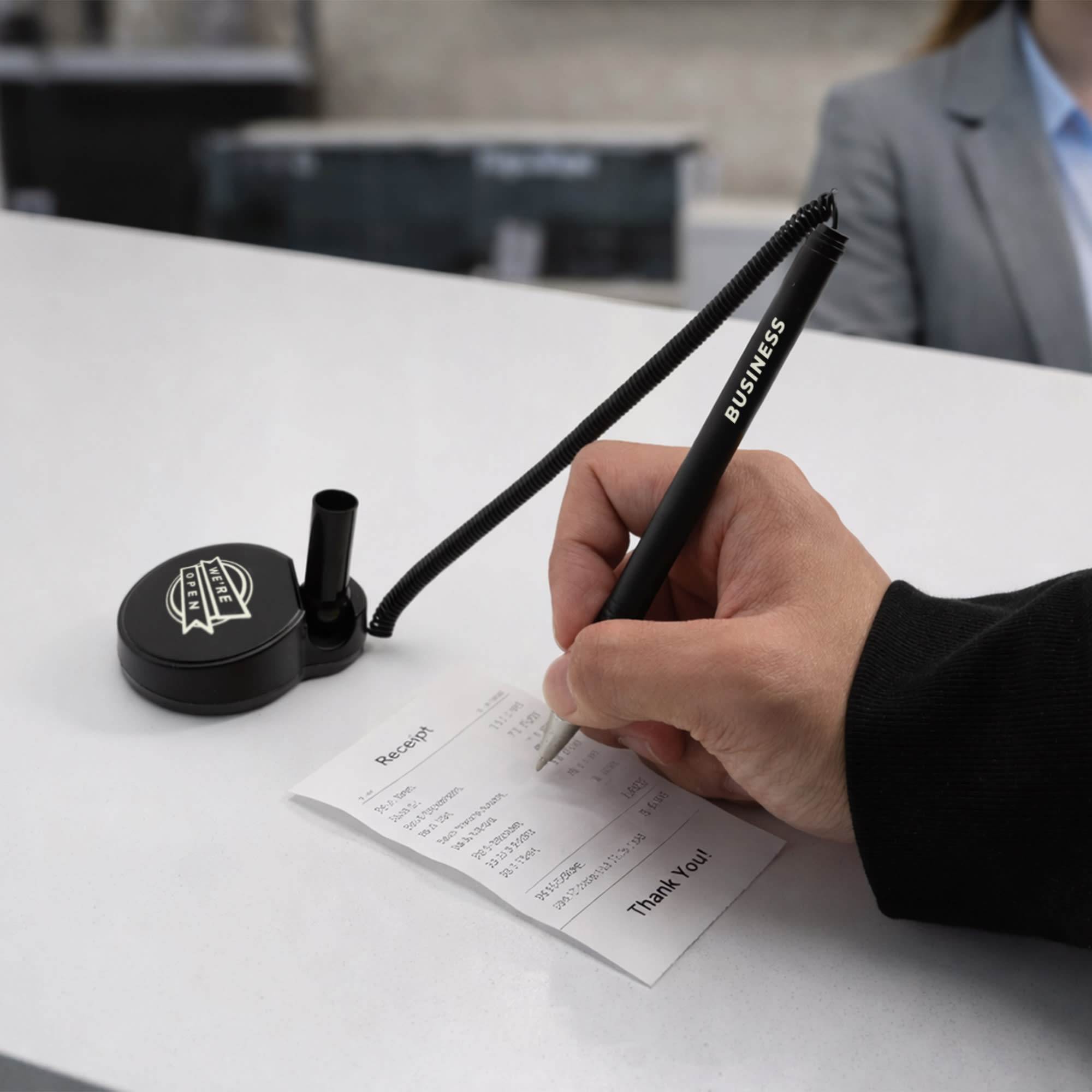 A black pen with a coil attached is being used to write on a receipt at a reception desk.