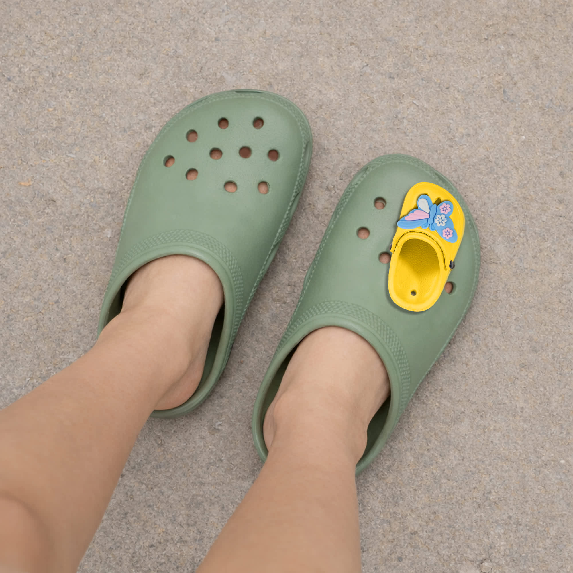 A pair of green clog shoes featuring a yellow paw-shaped charm on one side.