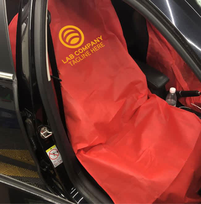 A red non-woven car seat cover with a logo, draped over the front seat of a car.