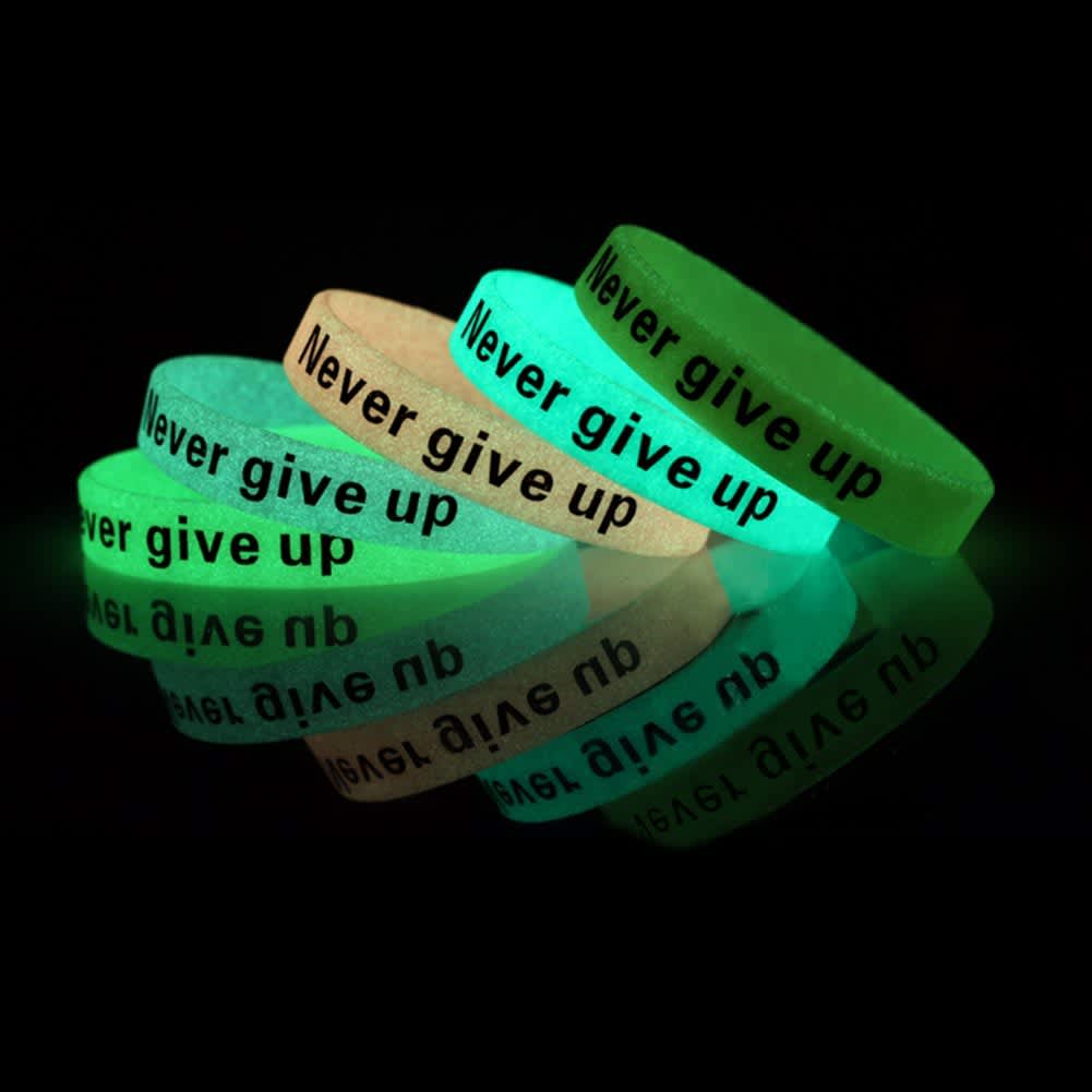 A set of glow-in-the-dark silicon wristbands in green and white with black text. They feature a motivational phrase.