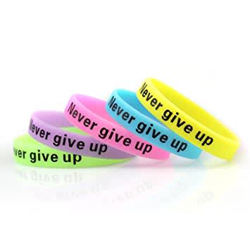 A collection of glow in the dark silicone wristbands in various colours with the phrase "Never give up" printed on them.