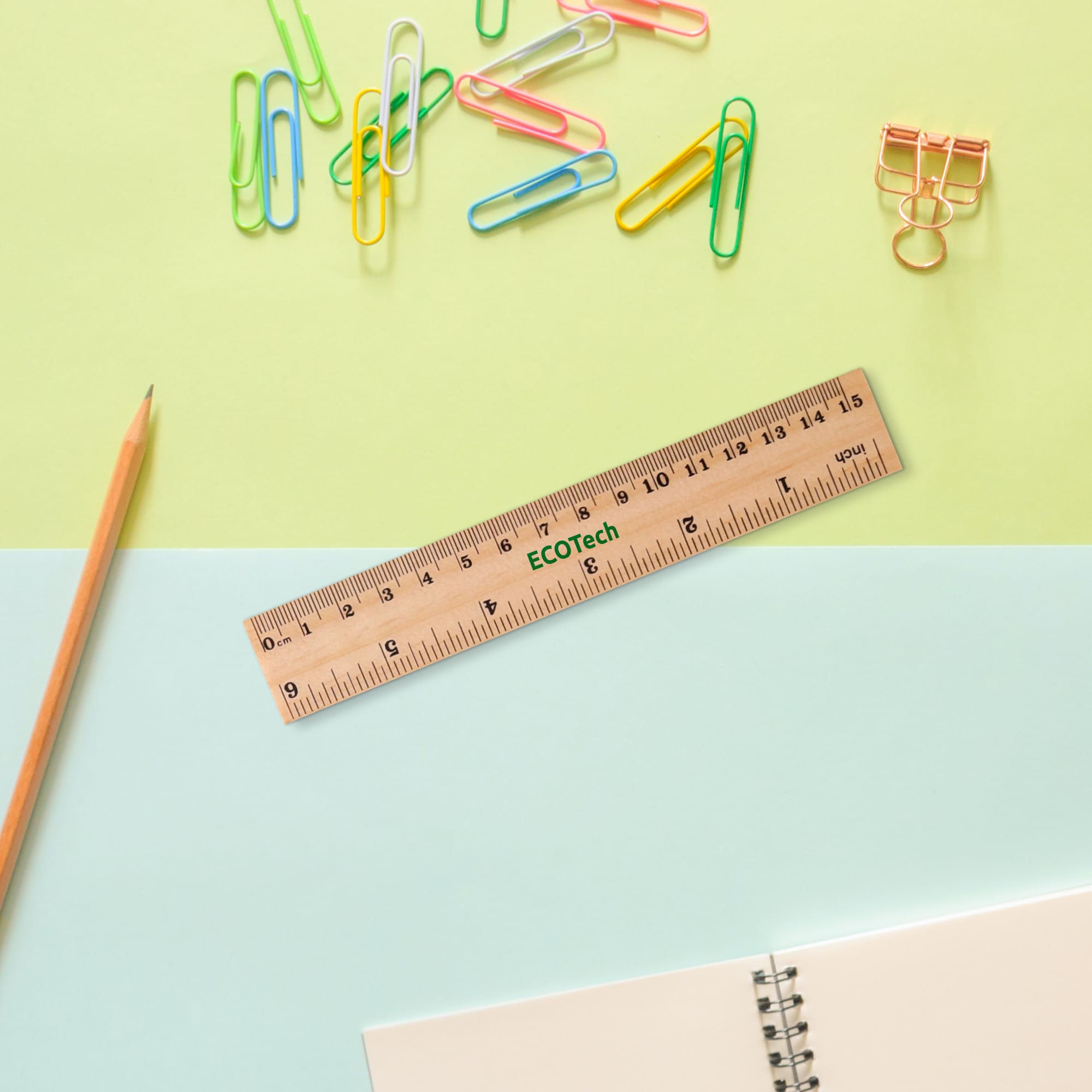 A wooden dual scale ruler rests on a blue and green background, surrounded by colourful paper clips and stationery items.