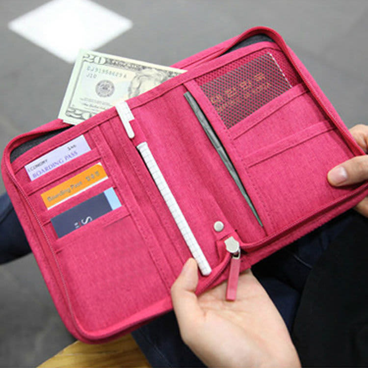 A pink passport holder opens to reveal compartments for cash, cards, and a pen, featuring a logo.