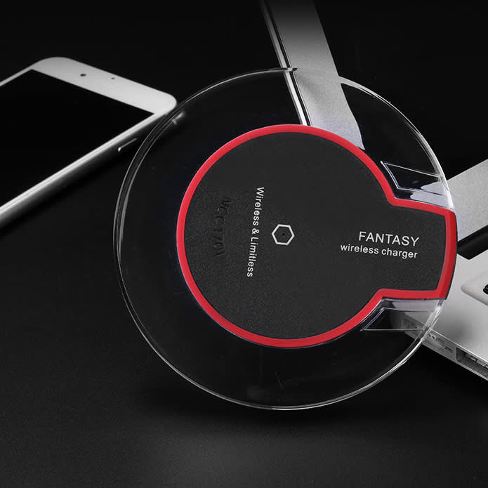 A circular wireless charger in black with red accents, positioned near a smartphone and laptop.