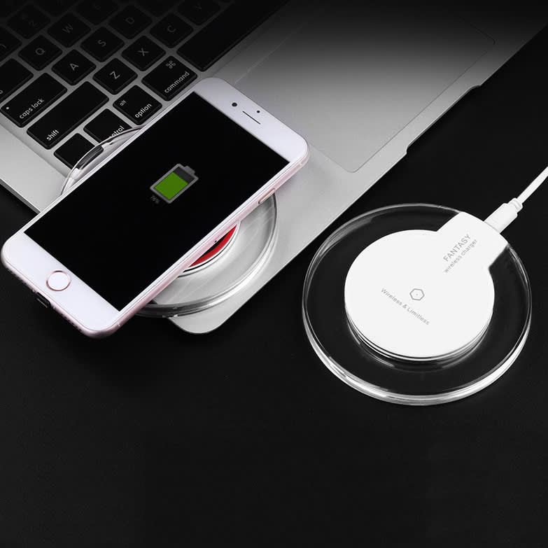A white wireless charger sits on a dark surface next to a smartphone displaying a low battery indicator.