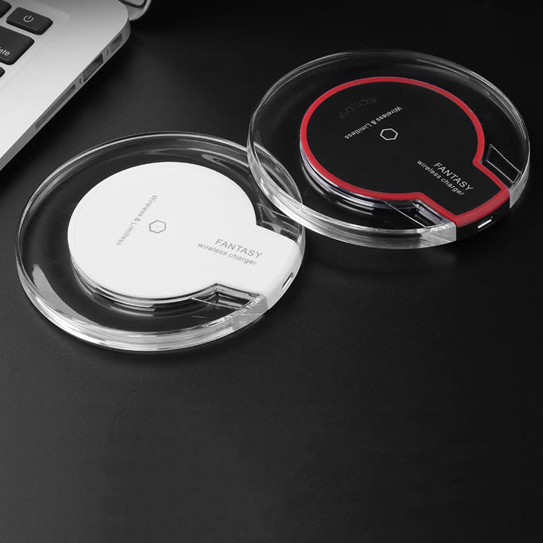A wireless charger set in white and black, featuring a sleek, transparent design, next to a laptop on a dark surface.