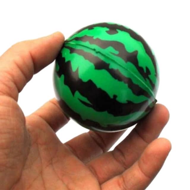 A hand holding a round stress reliever shaped like a watermelon, featuring green and black striped colouring.