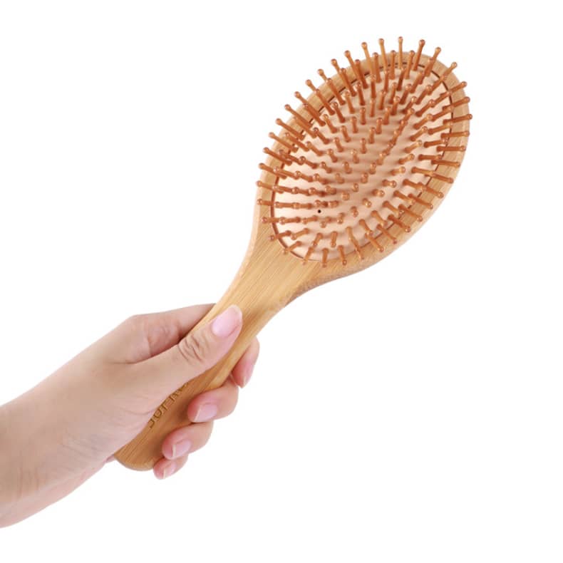 A bamboo airbag hair brush featuring a wooden handle and soft bristles, held in a hand.